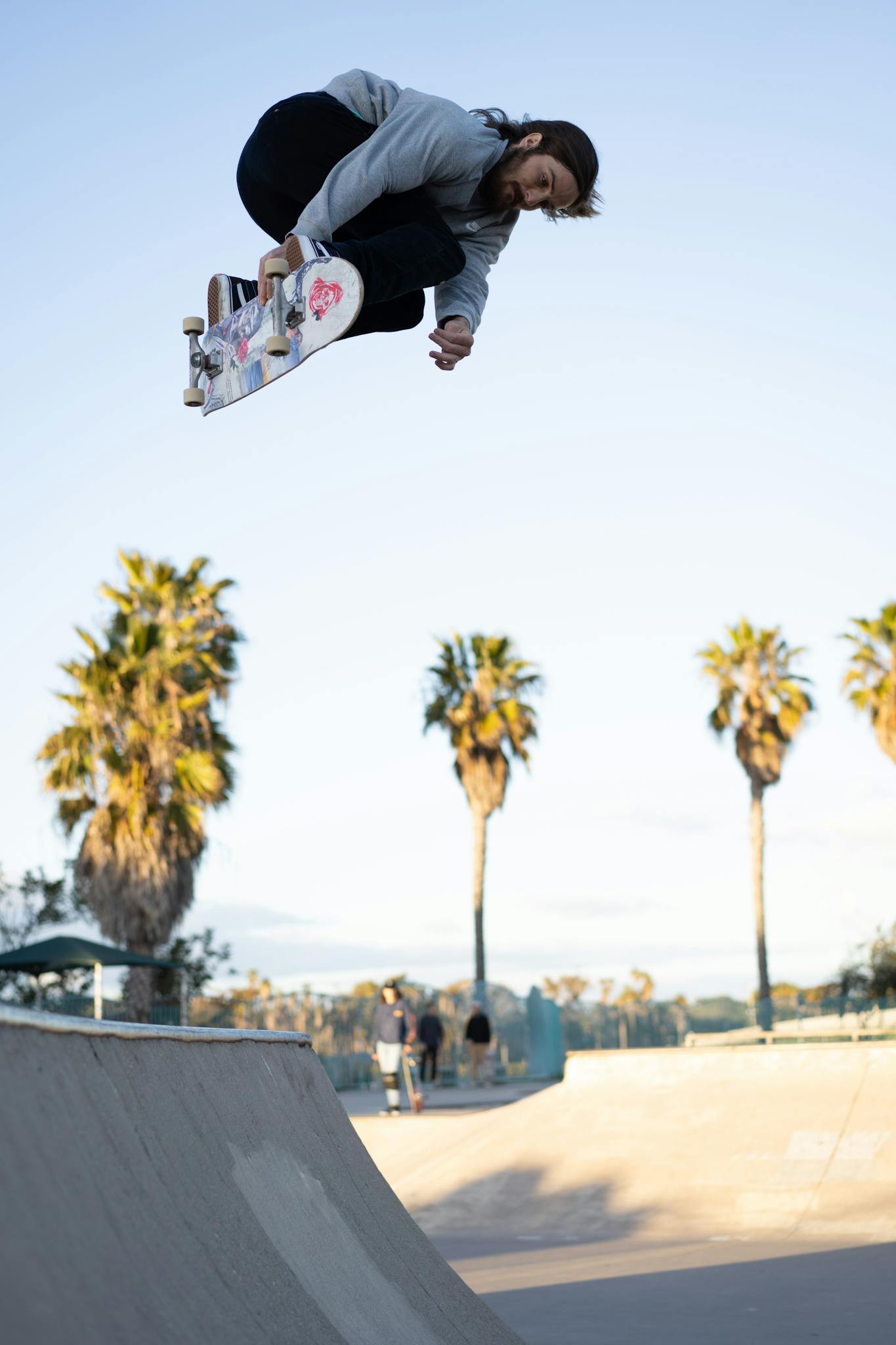 Skateboarder executing a high jump trick in a sunny outdoor park with palm trees.